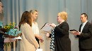 Tre kvinnor står på en scen med ett diplom