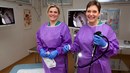 Två kvinnor står i vårdkläder i ett undersökningsrum med ett koloskop i handen