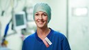 En kvinna i operationskläder står i en operationssal och tittar in i kameran.