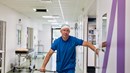 EN man i operationskläder och huva i en sjukhuskorridor.