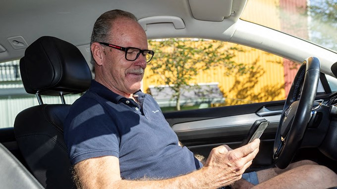 Bild på Jan-Ove Olsson som sitter i bilen och håller i sin mobiltelefon i handen.