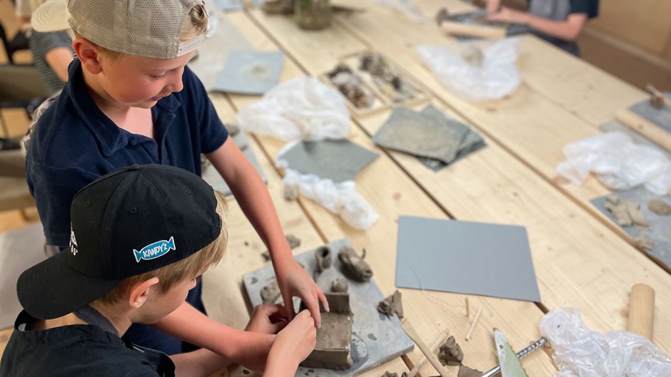 Två pojkar arbetar med händerna och designar med lera på bordet framför sig