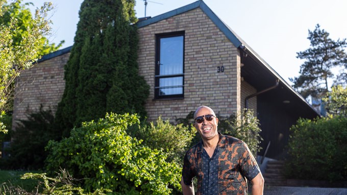 En man i solglasögon och skjorta står framför ett tegelhus.