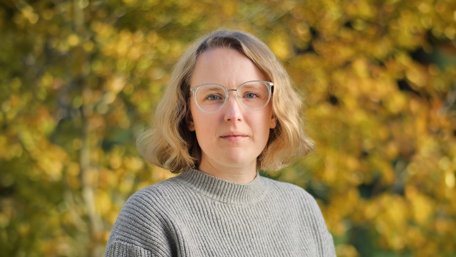Kvinna i glasögon står framför ett träd med gröngula löv