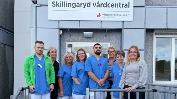 Sex kvinnor och två män i sjukvårdskläder står uppradade framför entrén till den tillfälliga paviljongen där Skillingaryd vårdcentral har sin verksamhet.