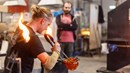 En glasblåsare i arbete. En person tittar på.