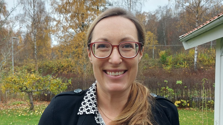 Kvinna med glasögon tittar in i kameran och ler.