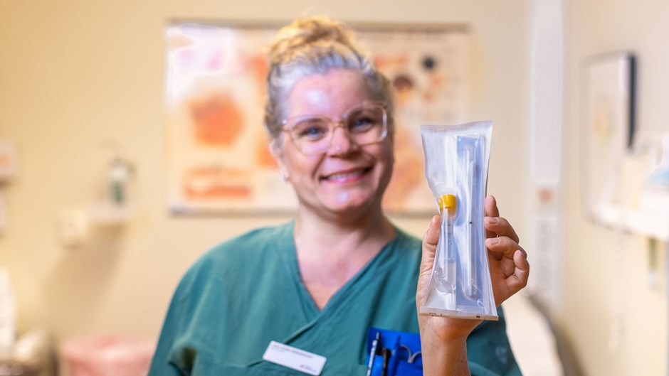 En kvinna i gröna sjukvårdskläder visar upp ett självprovtagningskit som ligger i en påse.