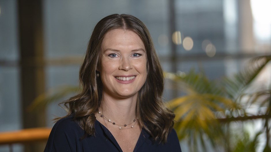 Mörkhårig kvinna som ler mot kameran med växter och glasrutor i bakgrunden.