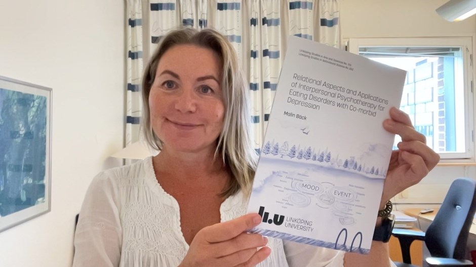 Kvinna i ett kontorsrum håller upp en tryckt doktorsavhandling.