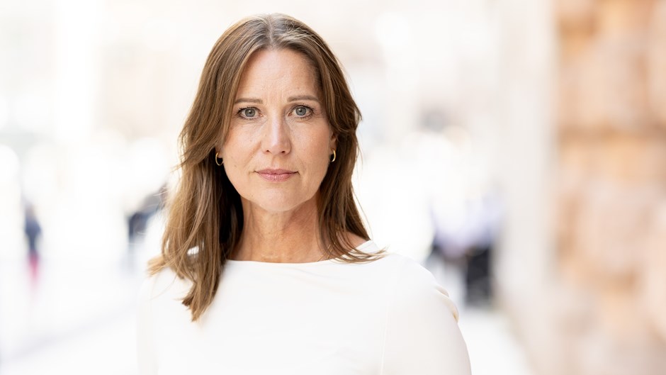 Mörkhårig kvinna med vit tröja står på en gata med tegel i bakgrunden.