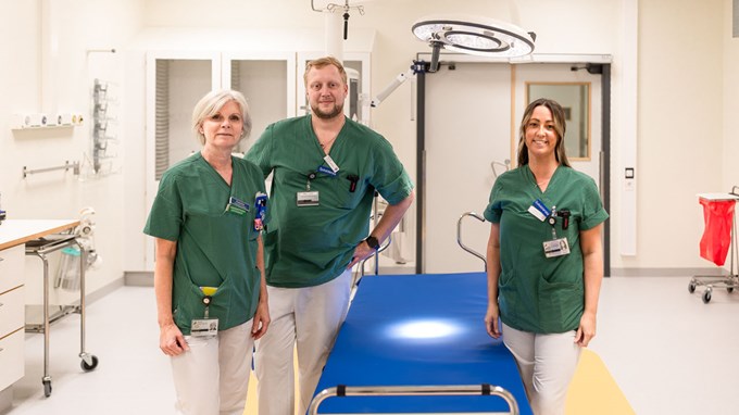 Tre personer står i en sjukhuslokal. De tre har gröna tröjor och vita byxor på sig.