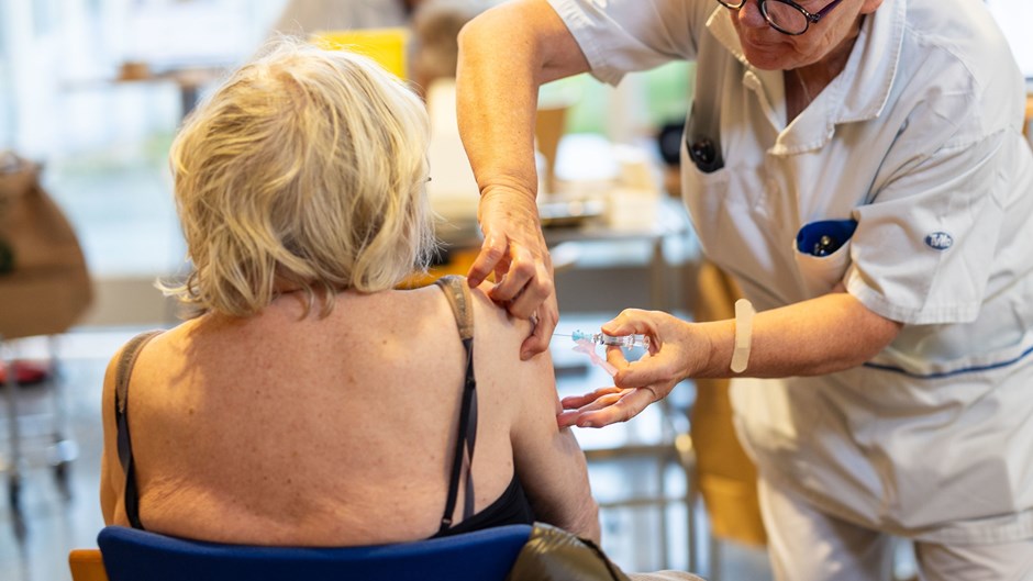 Sittande kvinna får en spruta i axeln av en kvinna i vita sjukvårdskläder.