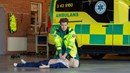 En person utför hjärt- och lungräddning på en docka. I bakgrunden syns en ambulans.