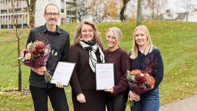 En man och tre kvinnor står utomhus och håller upp två blombuketter och två inramade motiveringar till pris.