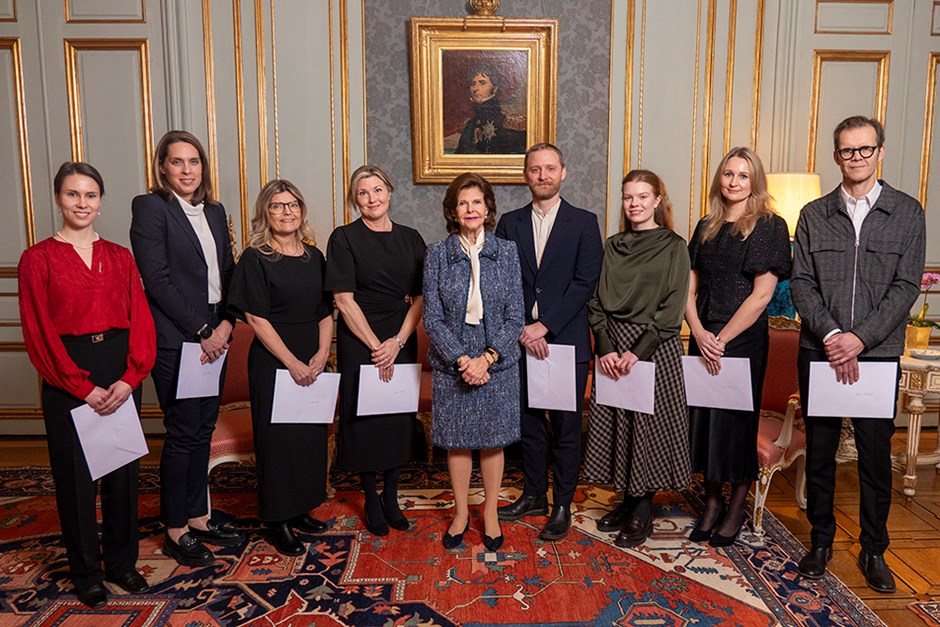 Nio personer står uppställa i ett rum och i mitten står drottning Silvia.