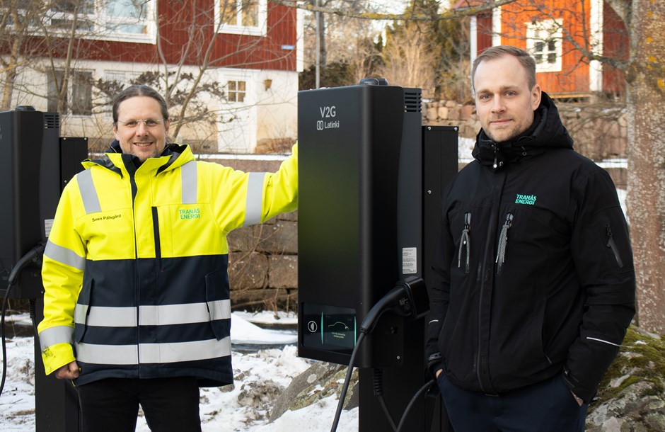 Två män står utomhus vid en svart laddstation för elbilar.