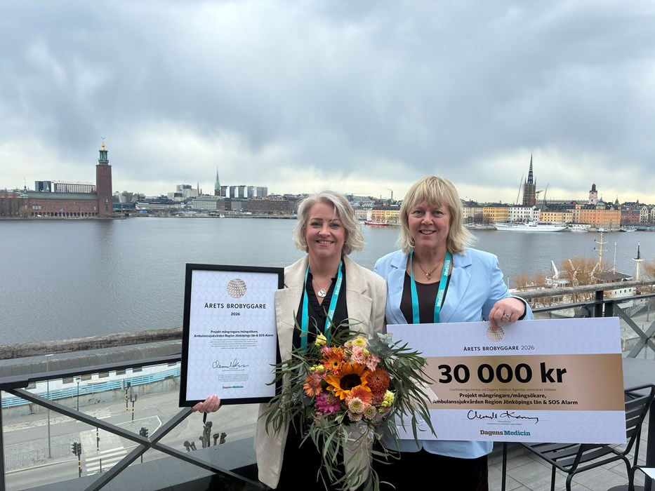Carola Söderberg, vårdutvecklare på SOS Alarm, och Annika Åström Victorén, överläkare inom ambulanssjukvården i Region Jönköpings län står på en takterrass med prischeck, blommor och diplom. Utsikt över Stockholm i bakgrunden.