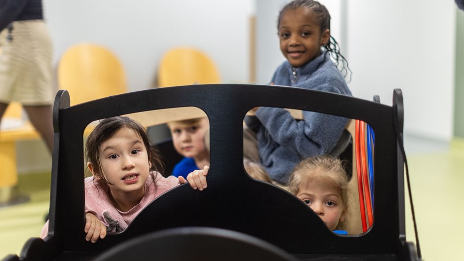 Fem barn sitter i en träbil i ett väntrum.