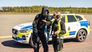 En polis står och pratar med en kvinna från räddningstjänsten. De båda står framför en polisbil.