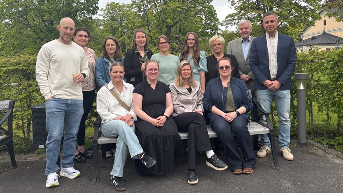 En gruppbild med totalt 14 personer. Tio personer står upp och fyra sitter på en bänk. Samtliga personer tittar in i kameran.