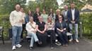 En gruppbild med totalt 14 personer. Tio personer står upp och fyra sitter på en bänk. Samtliga personer tittar in i kameran.