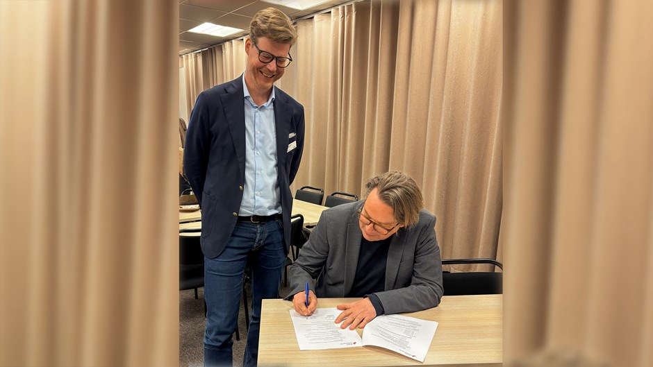 Två män i ett konferensrum. Den ena skriver på ett papper.