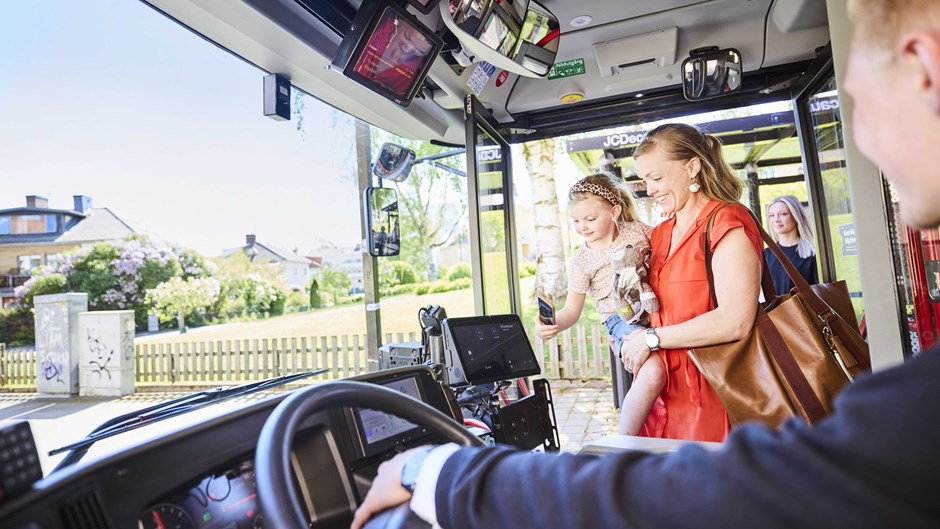 En kvinna med barn i famnen har precis gått på bussen och ska blippa biljett.