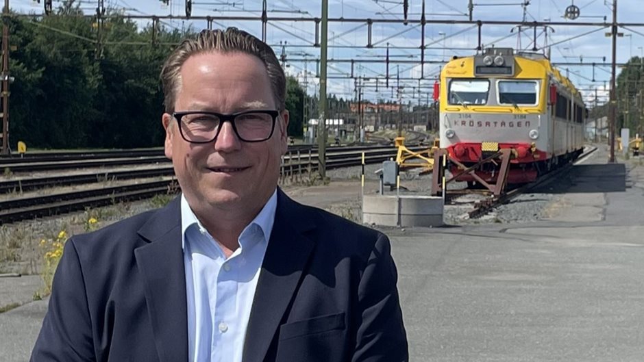 Man i kavaj med glasögon och ett tåg i bakgrunden.