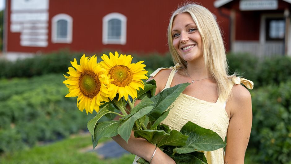 En ljushårig kvinna håller i flera solrosor.