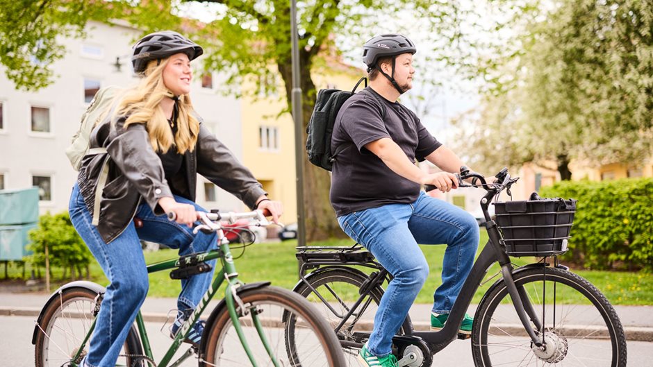 Två personer cyklar i stadsmiljö.