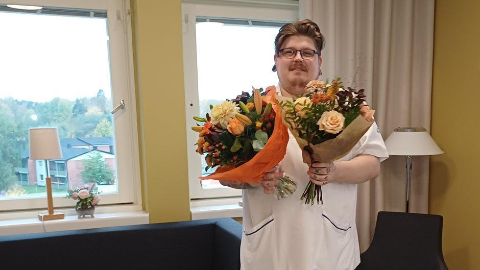 En man i vita kläder håller i två stora blombuketter.