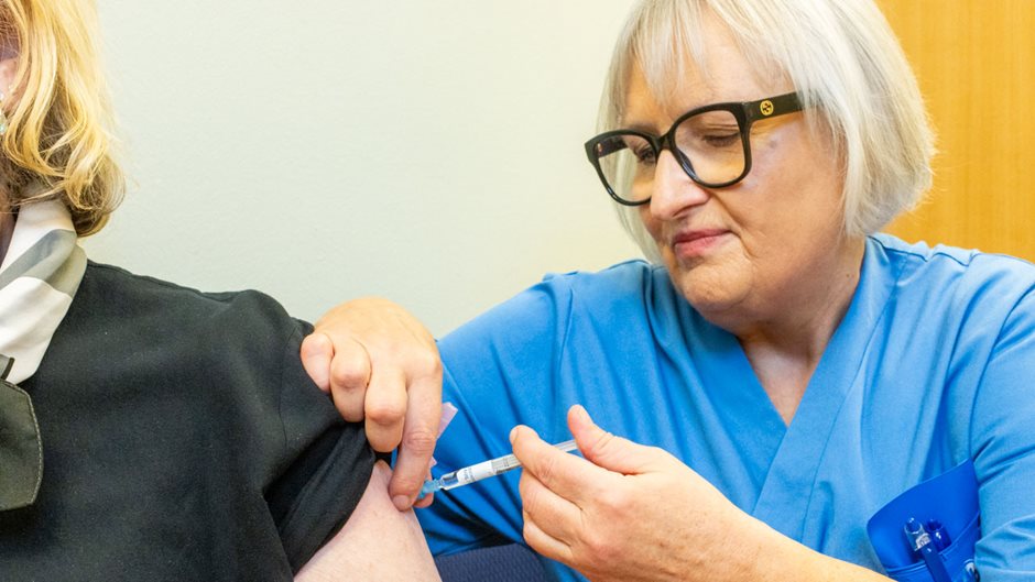 Kvinna i blå sjukvårdskläder ger en spruta i en patients arm.